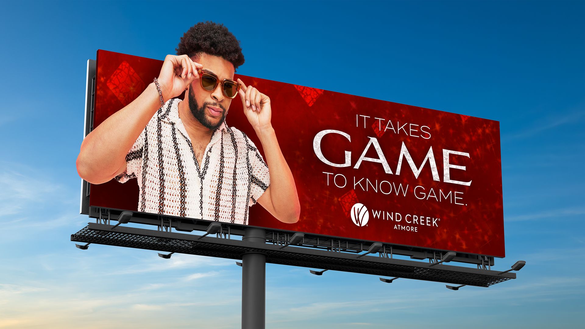 Billboard advertising Wind Creek Atmore with a man pulling down his sunglasses, with text 'IT TAKES GAME TO KNOW GAME.' and red diamond graphics.